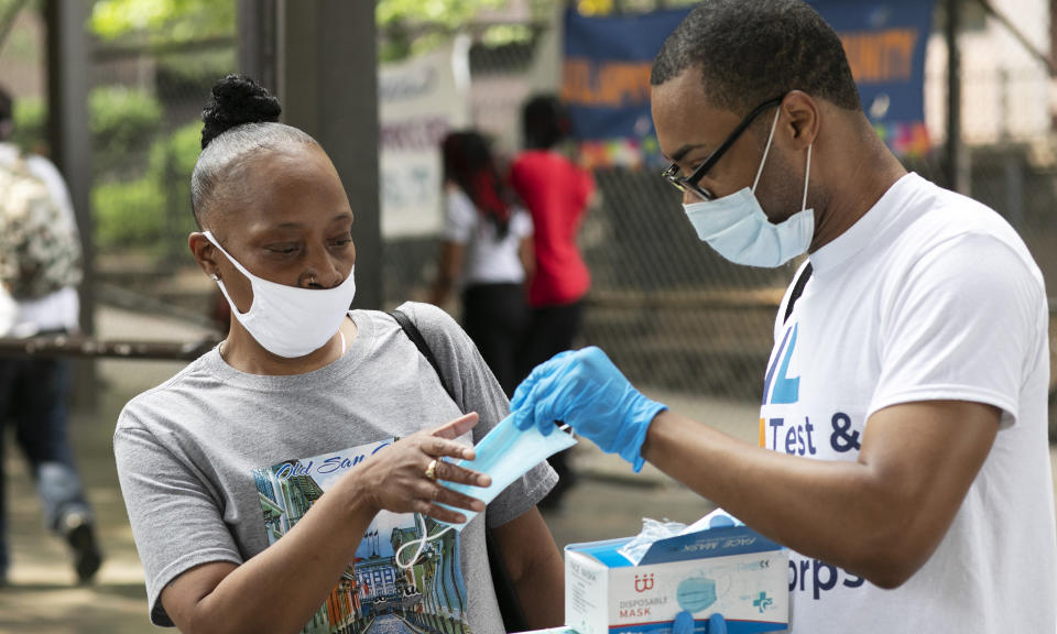 FILE - In this July 8, 2020, file photo, Stephane Labossiere, right, with the Mayor's Office of Immigrant Affairs, hands out masks and printed information about free COVID-19 testing in Brooklyn being offered by NYC Health + Hospitals, in New York. As coronavirus rages out of control in other parts of the U.S., New York is offering an example after taming the nation’s deadliest outbreak this spring — but also trying to prepare in case another surge comes. (AP Photo/Mark Lennihan, File)