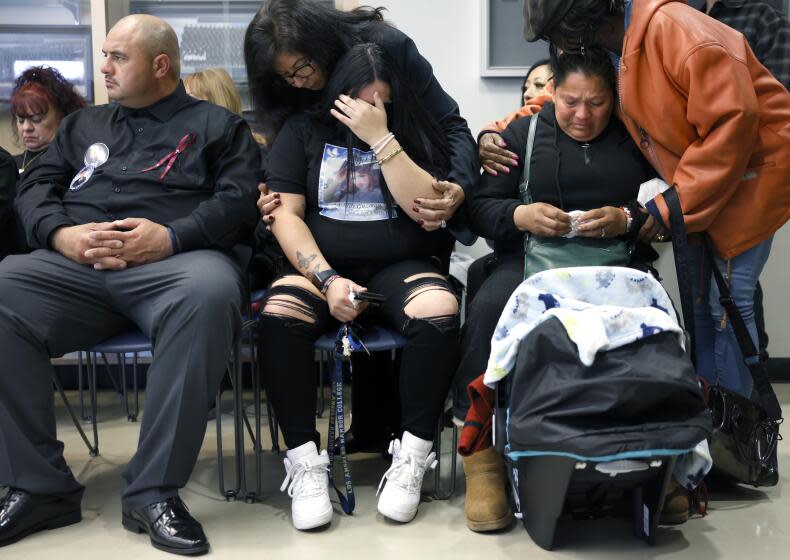 SAN PEDRO-CA-JANUARY 25, 2024: Vanessa Guzman, center, and Nora Galvan, right, are comforted as they mourn for their sister and daughter Ashley Guzman, during a gathering of families at the Harbor Area Community Police Station in San Pedro for a news conference announcing the arrest of a suspect in the shooting and killing of three victims, on January 25, 2024. Ashley Guzman and Carlos Loera were shot and killed in Harbor City on September 4, 2023. Their one-year-old child was also struck by the gunfire but survived his injuries. Joseph Saldana Sr., at left, wears a ribbon and photo pins on his shirt in honor of his son, Joseph Saldana, 17, a recent high school graduate who was shot and killed in San Pedro on September 30, 2023. (Christina House / Los Angeles Times)