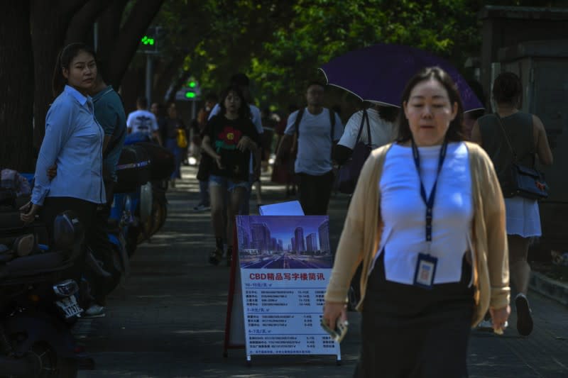 <cite>在北京的一條人行道上，一名房地產經紀人站在那里看著人們走過。中國經濟再顯疲緩，政府試圖安撫緊張不安的購房者。（AP）</cite>