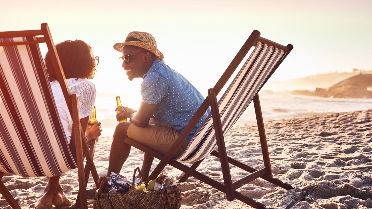 Shot of a happy young couple relaxing on chairs and having drinks at sunset on the beach.