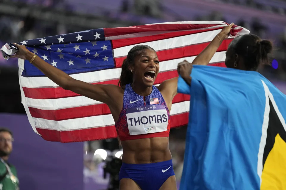 Gabby Thomas holds up the American flag in victory after winning a race.