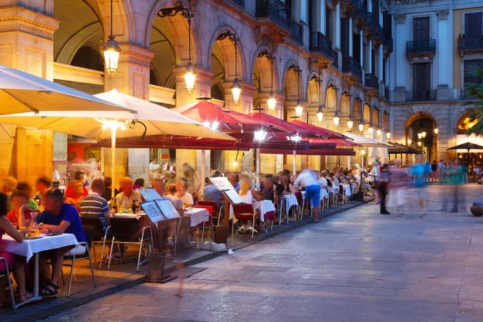 Outdoor café with patrons dining and walking in a European city's square at dusk