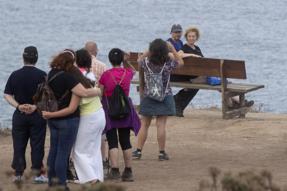 Varios turistas hacen cola, muy cerca el uno del otro, para tomarse una foto en un banco con el mar Cantábrico de fondo en Loiba, el noroeste de España, el 2 de agosto del 2020. (AP Photo/Paul White)