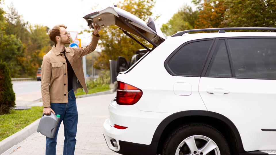 A man removing a container filled with engine oil from the trunk of his car