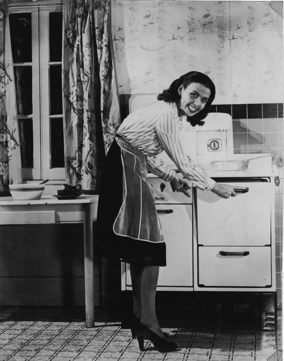 <p>The singer and actress checks on the meal that's cooking in her oven while in her kitchen in 1940. </p>