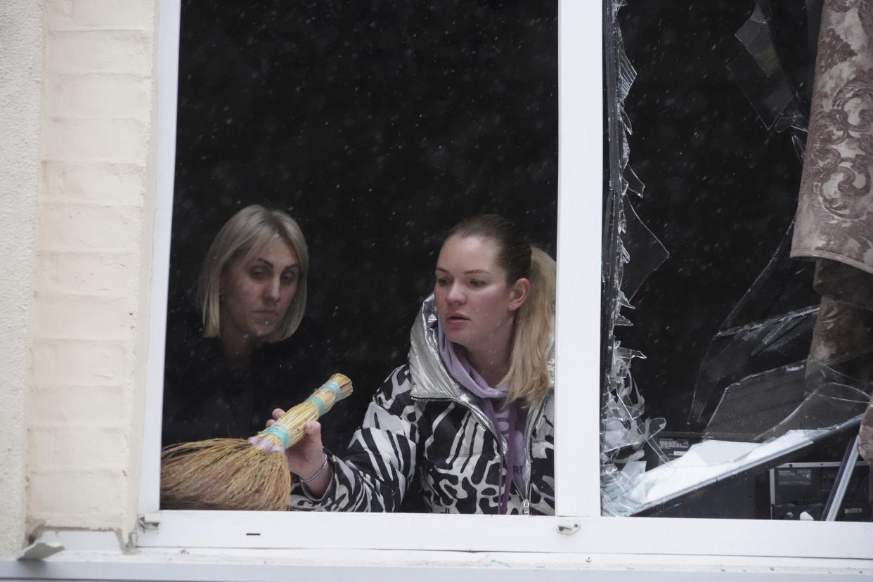 Women clean up broken glass from the window of a residential building which was hit by a Russian rocket, in the city center of Kharkiv, Ukraine, Sunday, Feb. 5, 2023. (AP Photo/Andrii Marienko)