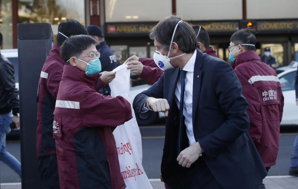 Vice President of Region Lombardy Fabrizio Sala, right, salutes with his forearm medics and paramedics from China upon arrival at the Malpensa airport of Milan, Wednesday, March 18, 2020. Some 37 between doctors and paramedics were sent along with some 20 tons of equipment, and will be deployed to different hospitals in Italy's most affected area. For most people, the new coronavirus causes only mild or moderate symptoms. For some it can cause more severe illness, especially in older adults and people with existing health problems. (AP Photo/Antonio Calanni)
