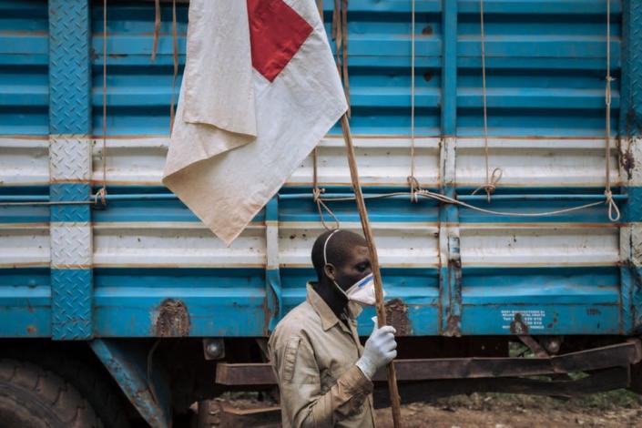 A Red Cross volunteer holds a Red-cross flag while his colleagues bury the bodies of people killed by Codeco militiamen in the village of Dhedja, December 19, 2021, 60 kilometers from Bunia, the provincial capital of Ituri in northeastern Democratic Republic of Congo