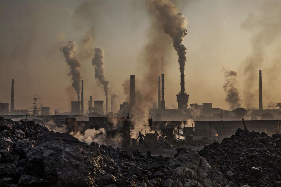 Smoke billows from a large steel plant as a Chinese labourer works at an unauthorized steel factory, foreground, on Nov. 4, 2016, in Inner Mongolia, China.