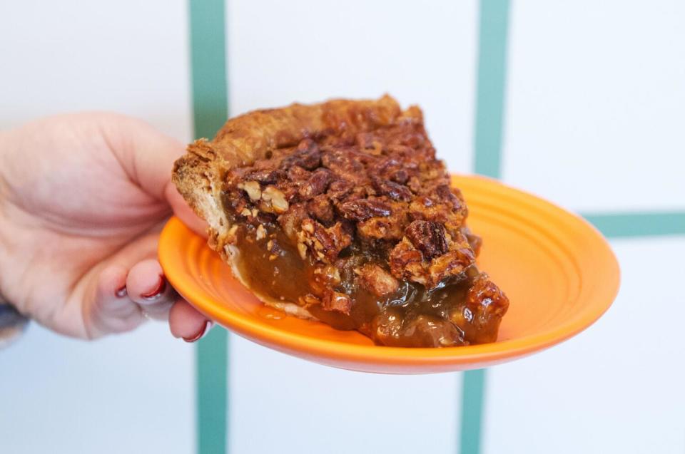 A hand holds a slice of pumpkin pie on an orange plate at Culver City's Fat + Flour cafe