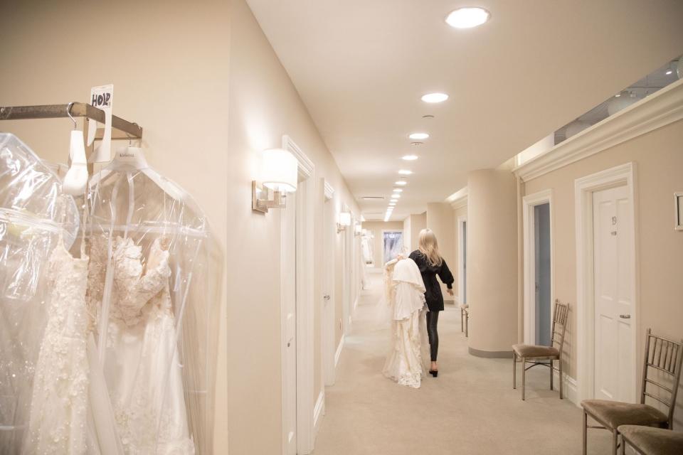 A woman walks down a hallway with doors carrying a wedding dress.