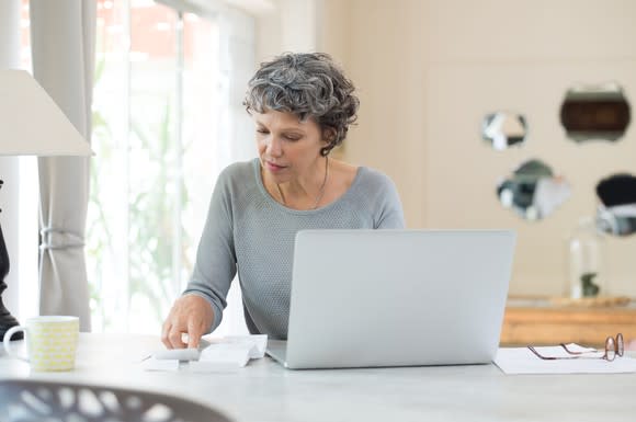 Older woman at a laptop with papers and receipts