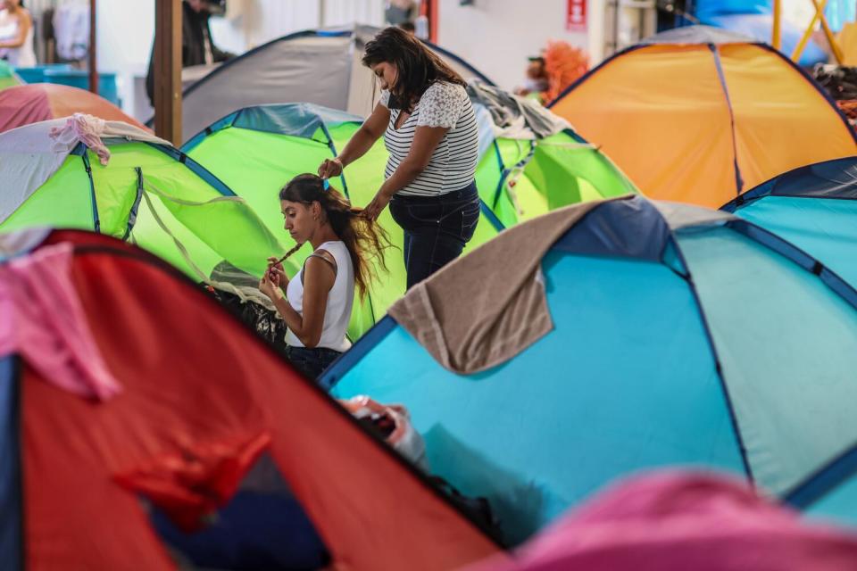 A woman combs or adjusts a girl or woman's hair among tents.