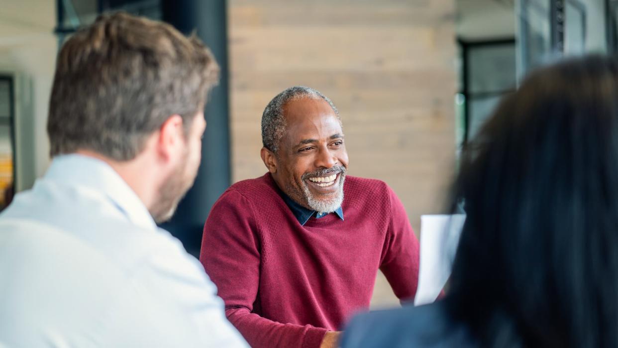 Smiling mature male manager sitting with colleagues in board room.