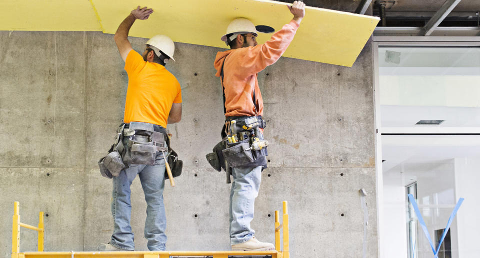 Two construction workers install insulation inside a warehouse.