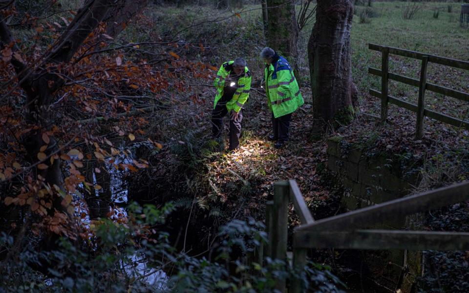 Police officers arrive before sunrise to search the water filled gulley where the crash is believed to have happened
