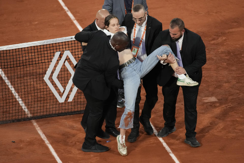 A climate activist is carried off after she tied herself to the net during the semifinal match between Croatia's Marin Cilic and Norway's Casper Ruud at the French Open tennis tournament in Roland Garros stadium in Paris, France, Friday, June 3, 2022. (AP Photo/Christophe Ena)