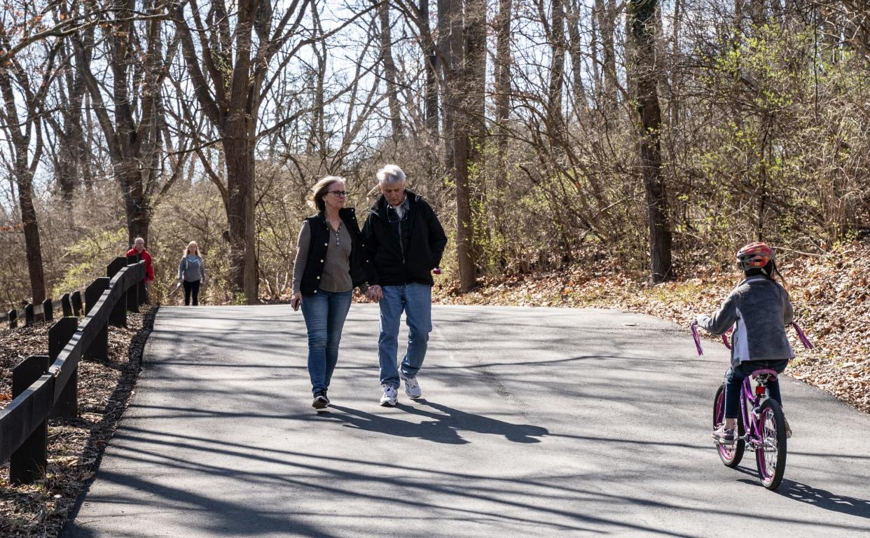 Berks County, Pennsylvania, USA-March 15, 2020:  Senior couple walks holding hands as a young bike rider passes. People have been asked to social distance to prevent spread of coronavius which can be difficult when walking in park.