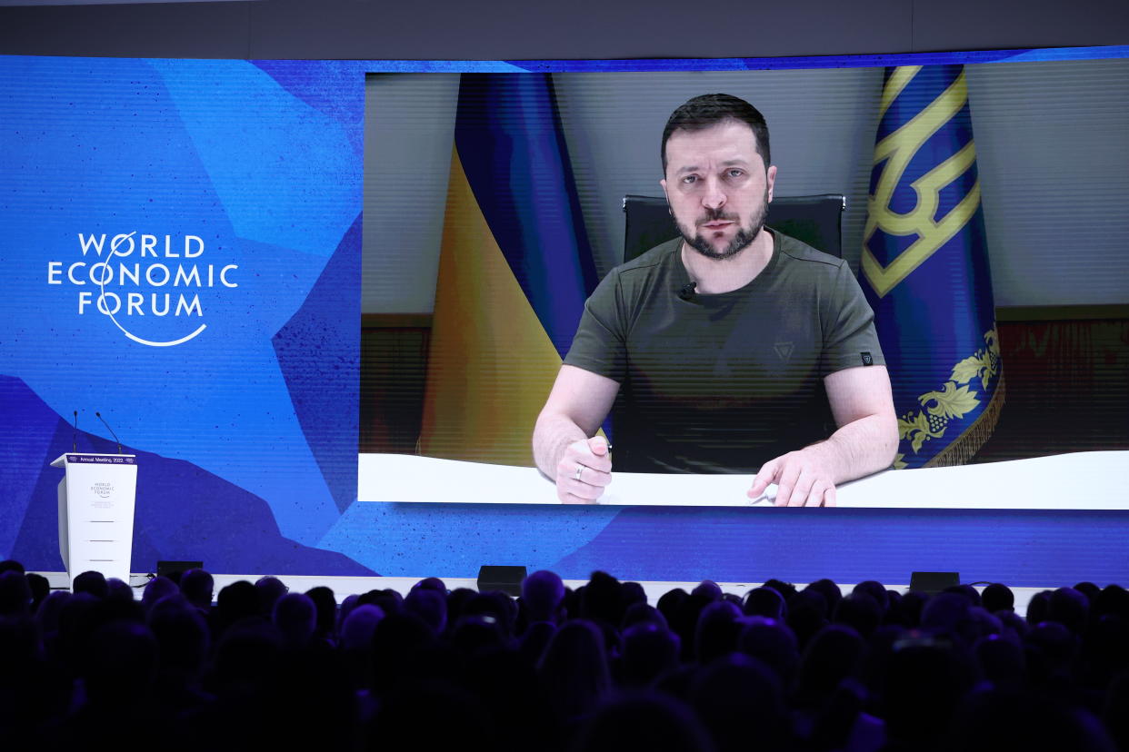 President Volodymyr Zelensky, in gray T-shirt, speaks to a large audience in Davos on a video screen.