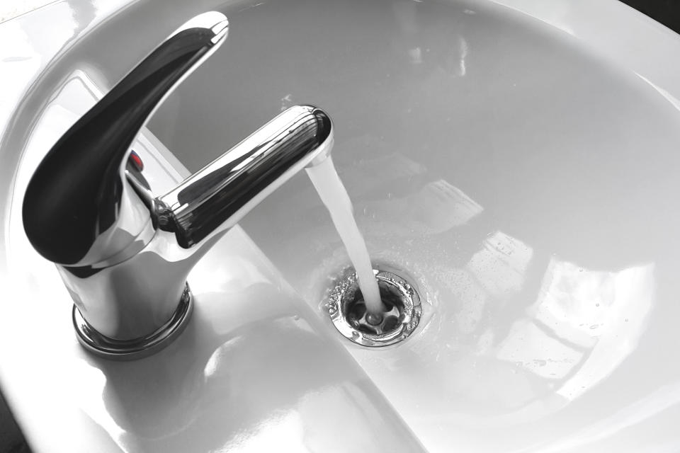 Water tap faucet with flowing water in a white bathroom sink.