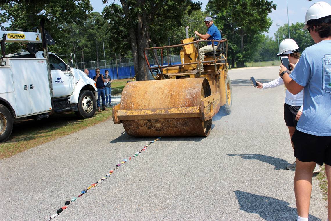 Jason Thomason, of Wellons Construction, rolls over a line of vaping devices with a steel drum roller near the baseball field at Triton High School. Micheal Cole and Hunter Thompson, at right, record a video of the destruction.