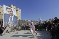 Syrians perform in front of a large poster of President Bashar al-Assad outside the Aleppo Citadel on January 22, 2017