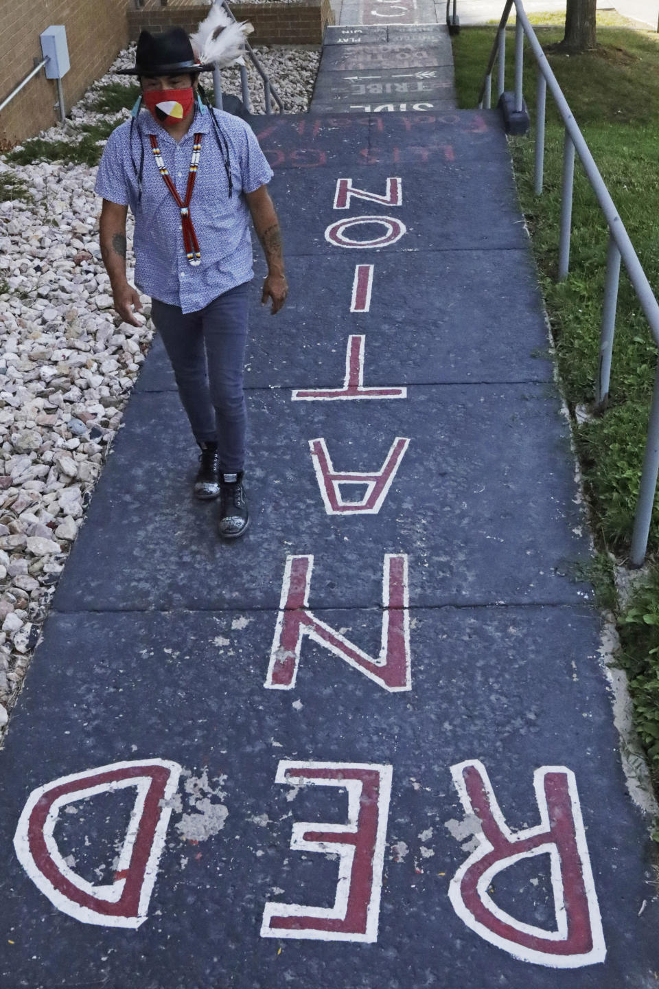 Native American advocate Carl Moore walks along a walkway which leads from the Bountiful High School parking lot up to the football field Tuesday, July 28, 2020, in Bountiful, Utah. While advocates have made strides in getting Native American symbols and names changed in sports, they say there's still work to do mainly at the high school level, where mascots like Braves, Indians, Warriors, Chiefs and Redskins persist. (AP Photo/Rick Bowmer)