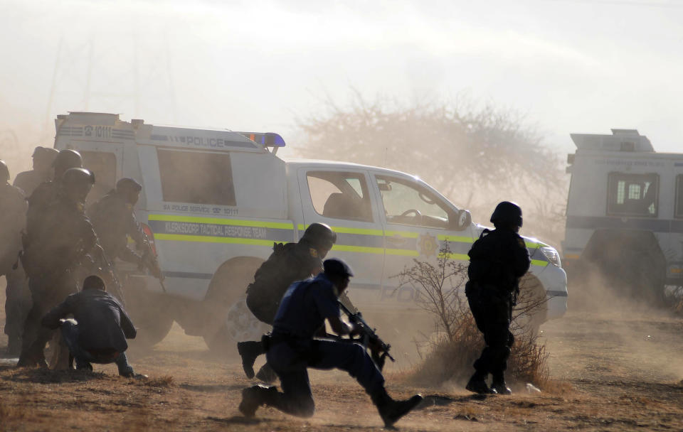 Policemen in teargas and dust open fire on striking miners at the Lonmin Platinum Mine near Rustenburg, South Africa, Thursday, Aug. 16, 2012. South African police opened fire Thursday on a crowd of striking workers at a platinum mine, leaving an unknown number of people injured and possibly dead. Motionless bodies lay on the ground in pools of blood. (AP Photo)