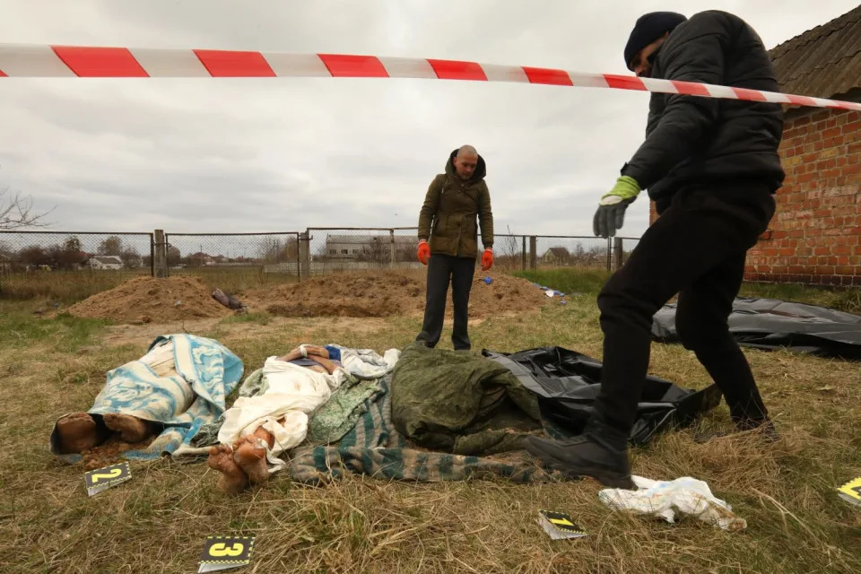 People stand looking over bodies on the ground