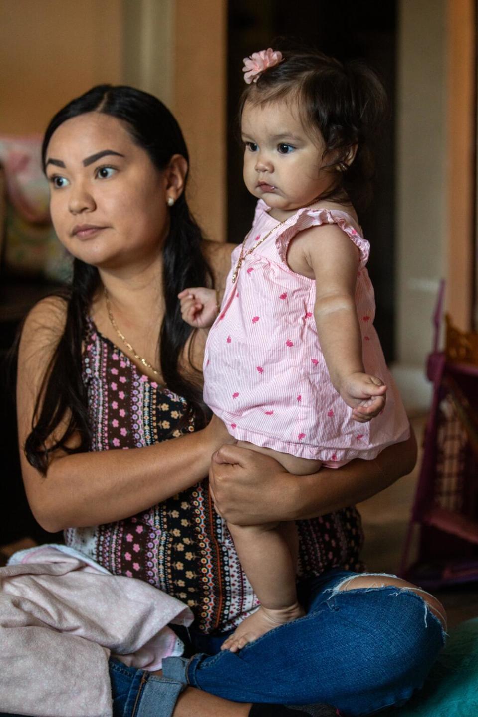 A woman with long dark hair holds a baby girl in a pink outfit