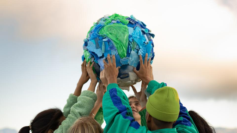 a group of teenagers hold up a model of planet earth made of plastic.