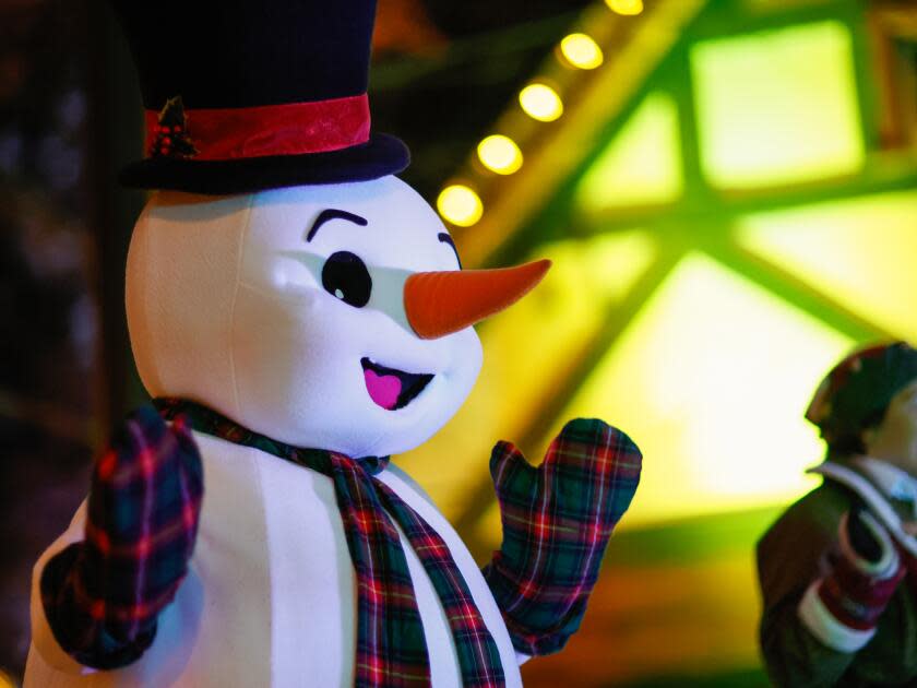 A person in a snowman costume walking around a Christmas village at night.