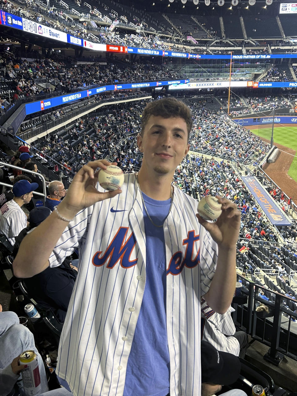 In a photo provided by Jerry Beach, Patrick Wedderburn holds up two foul falls he caught during a three-pitch span at a baseball game between the Cincinnati Reds and the New York Mets on Friday, Sept. 15, 2023, in New York. (Jerry Beach via AP)