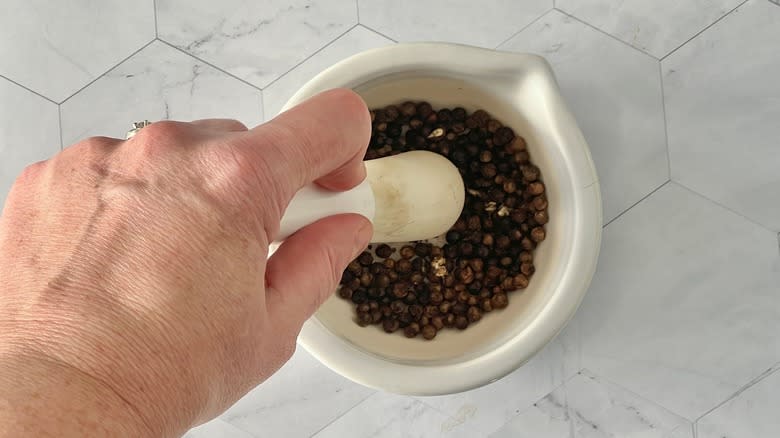 hand crushing black peppercorns in mortar and pestle