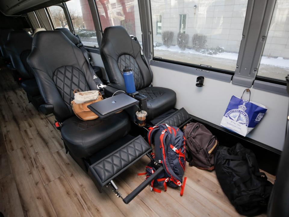 A row of two leather sets. One chair has a laptop, purse, water bottle with bags on the floor.