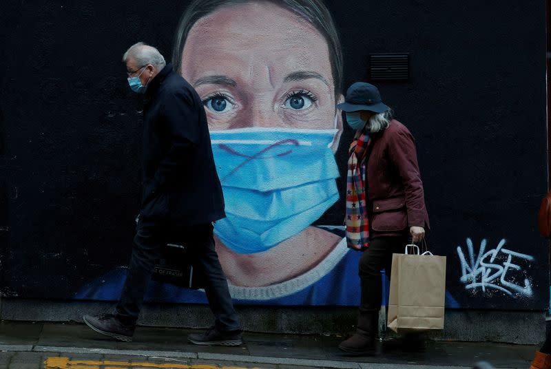 FILE PHOTO: People wearing face masks walk past a mural of a nurse in the centre of Manchester