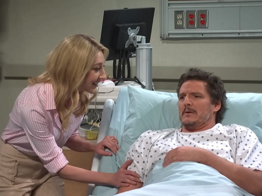 pedro pascal on saturday night live, acting as a coma patient who has just woken up. he's in a hospital gown and laying on a bed, looking very confused and concerned