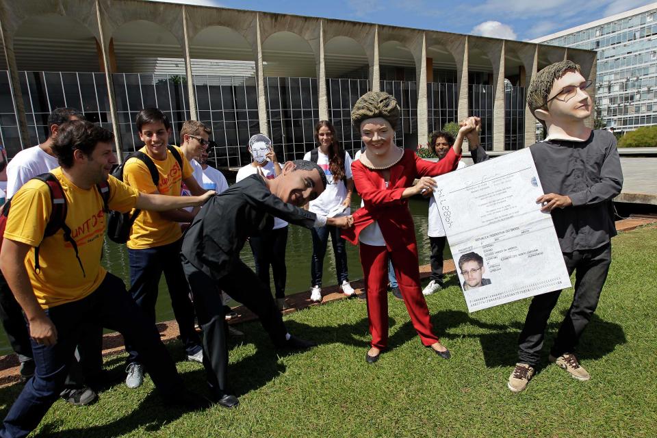 Activistas con máscaras que representan al presidente de EEUU Barack Obama, izquierda; a la presidenta brasileña Dilma Rousseff, centro, y al exanalista estadounidense de inteligencia Edward Snowden sostienen una pancarta que imita el pasaporte de Snowden en las afueras del ministerio de Relaciones Exteriores en Brasilia, Brasil, el jueves 13 de febrero de 2014. Activistas y actores entregaron en la cancillería una petición con más de un millón de firmas para que Brasil le conceda asilo al exanalista norteamericano. (AP Photo/Eraldo Peres)