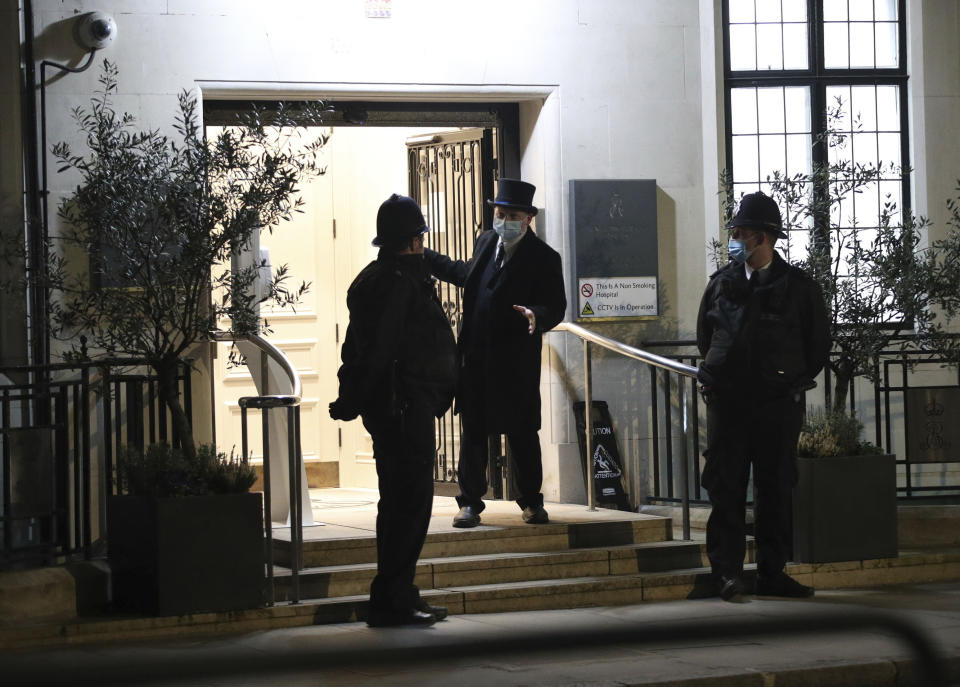 Police officers and a doorman outside the King Edward VII's hospital in London, Thursday, Feb. 18, 2021. Buckingham Palace said the husband of Queen Elizabeth II, 99-year-old Prince Philip was admitted to the private King Edward VII Hospital on Tuesday evening after feeling unwell. (Yui Mok/PA via AP)