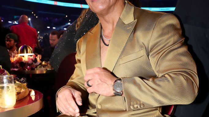 dwayne johnson sitting at his table at the grammy awards and wearing a gold suit