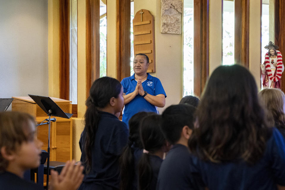 Sacred Hearts School Principal Tonata Lolesio leads a prayer during an assembly at Sacred Hearts Mission Church on Tuesday, Oct. 3, 2023, in Lahaina, Hawaii. Sacred Hearts School, a Catholic school, was founded in 1862. Most of the school burned down, but its leaders quickly got classes up and running at Sacred Hearts Mission Church 10 miles (16 kilometers) away. (AP Photo/Mengshin Lin)