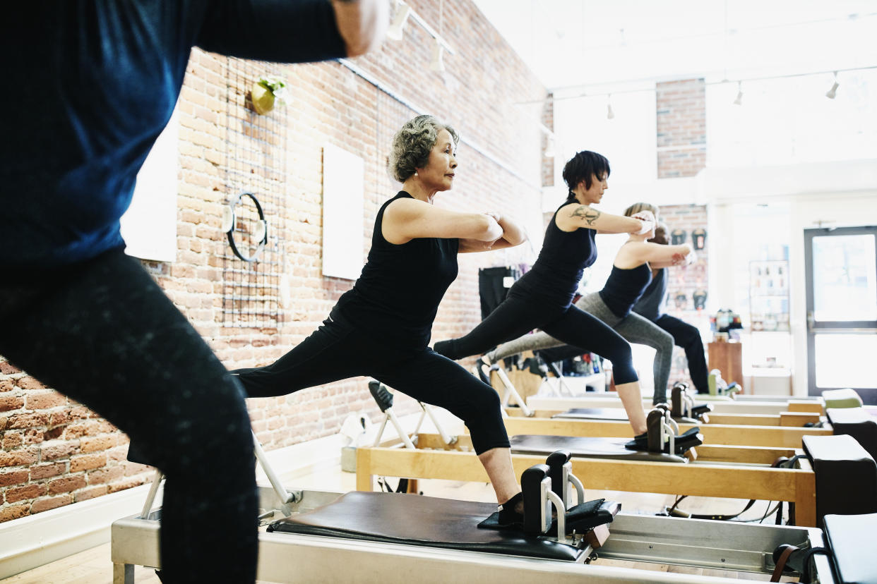 Mature woman balancing on reformer while doing roman splits during class in pilates studio