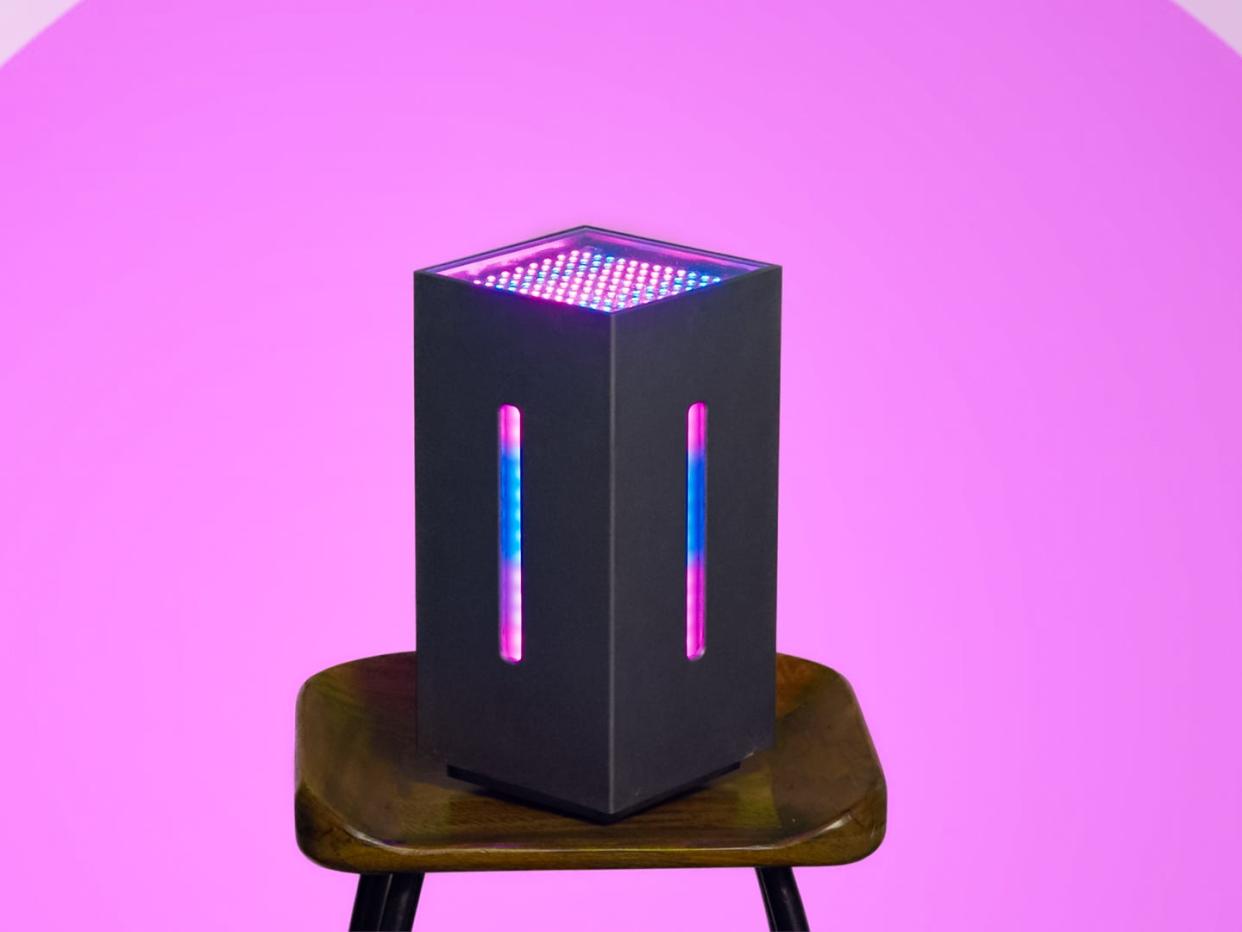 a computer tower with blue and pink lights from the circle, sitting on a stool in front of a pink background