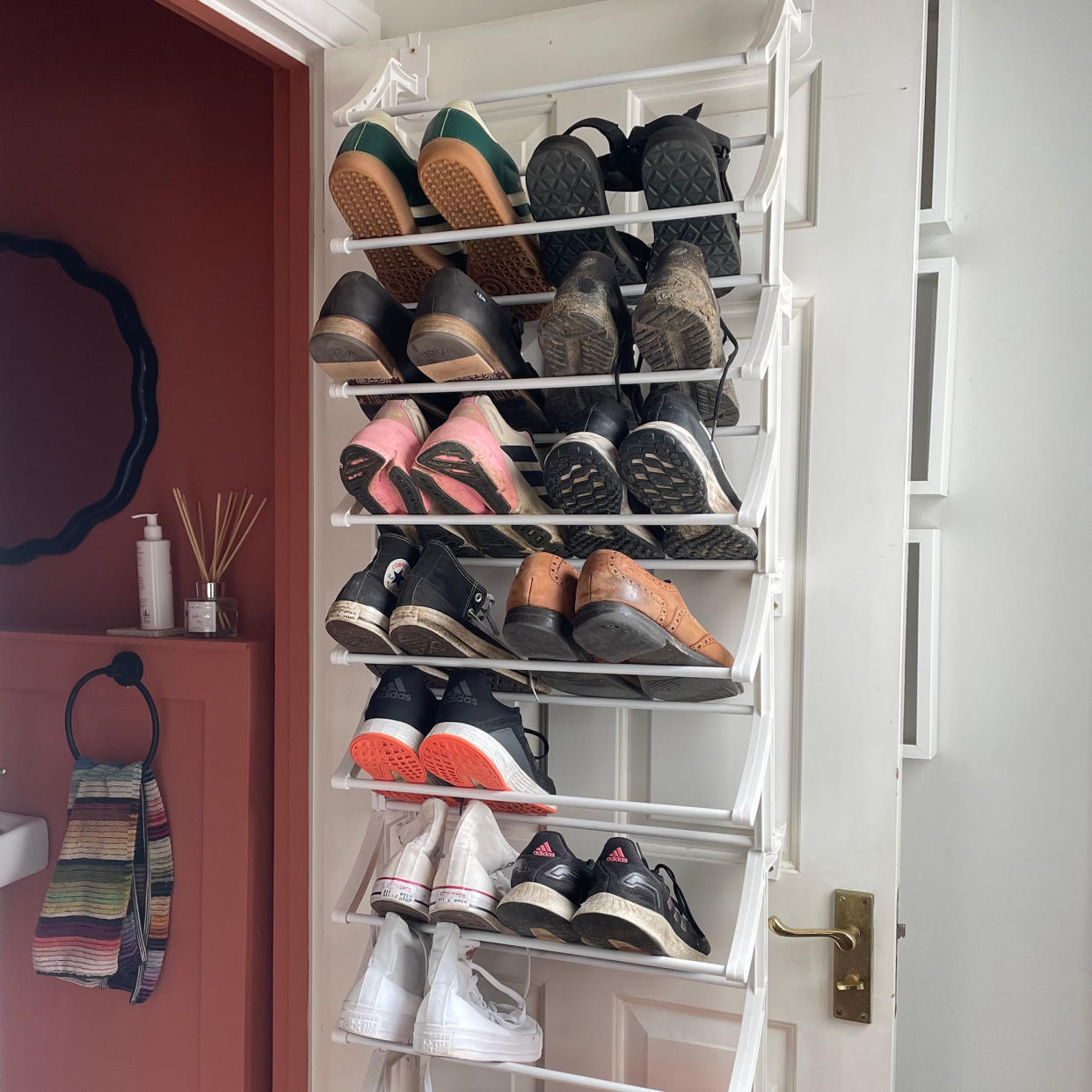  White door with a white shelving rack holding shoes and trainers with a glimpse of a red bathroom behind. 