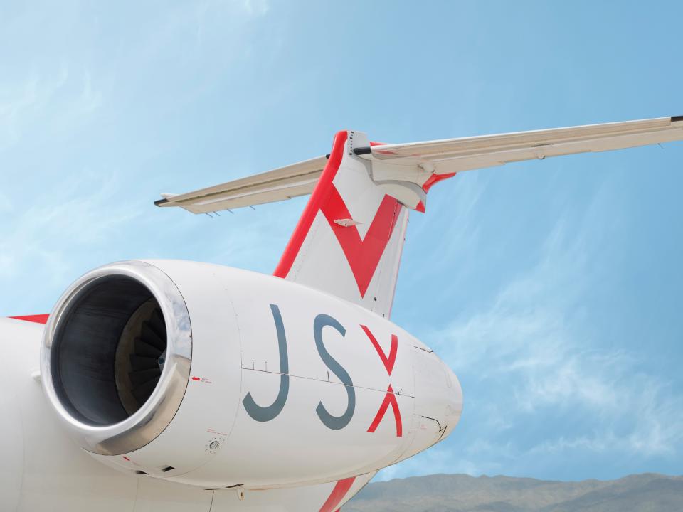 The engine and tail-end of a JSX jet in front of a clear sky.