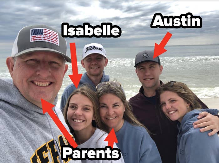 Group of five smiling people taking a selfie on a beach; two men wearing caps, two women with sunglasses atop heads, one woman in center