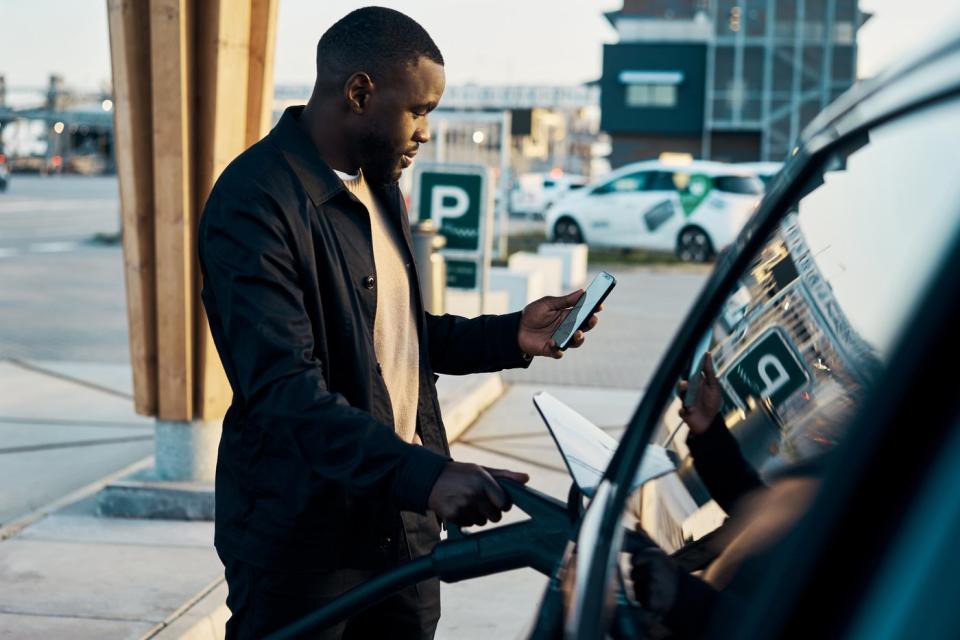 Person charging his electric vehicle while looking at a mobile phone. 