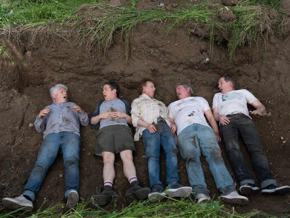 Five men lay side by side in a shallow pit of dirt.