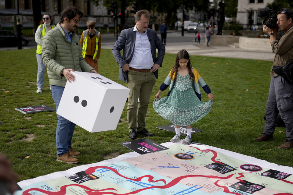 Richard Ratcliffe, the husband of imprisoned British-Iranian Nazanin Zaghari-Ratcliffe, center, and their seven year old daughter Gabriella stand by a giant snakes and ladders board in Parliament Square, London, to show the "ups and downs" of Zaghari-Ratcliffe's case to mark the 2,000 days she has been detained in Iran, Thursday, Sept. 23, 2021. Zaghari-Ratcliffe was originally sentenced to five years in prison after being convicted of plotting the overthrow of Iran's government, a charge that she, her supporters and rights groups deny. While employed at the Thomson Reuters Foundation, the charitable arm of the news agency, she was taken into custody at the Tehran airport in April 2016 as she was returning home to Britain after visiting family. (AP Photo/Matt Dunham)