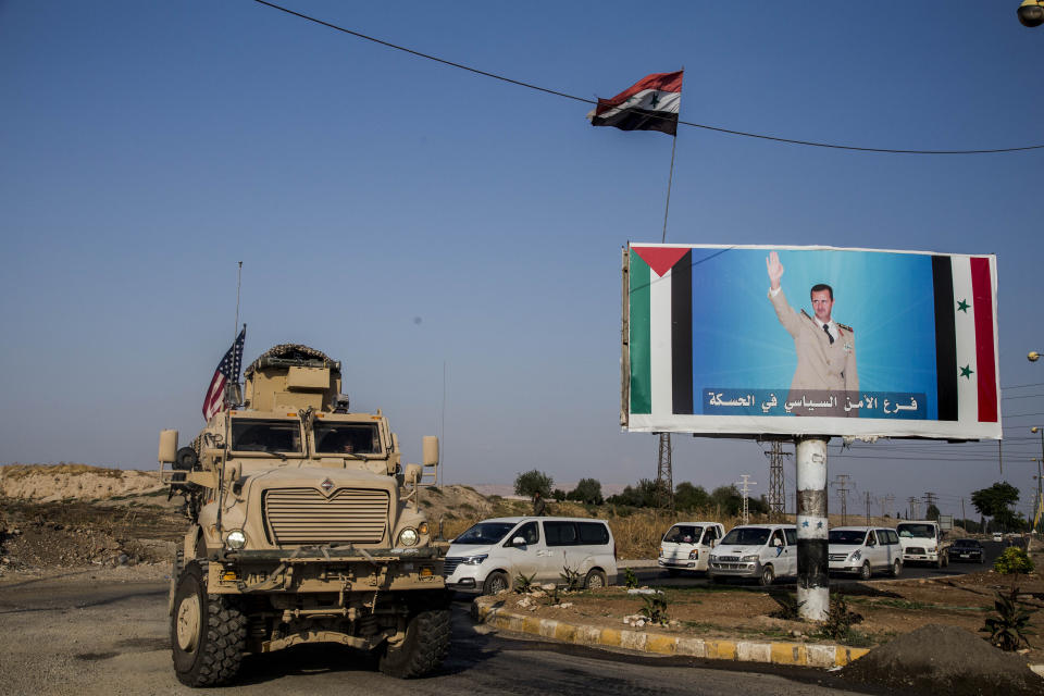 U.S. military convoy drives the he town of Qamishli, north Syria, by a poster showing Syrain President Bashar Aassad Saturday, Oct. 26. 2019. A U.S. convoy of over a dozen vehicles was spotted driving south of the northeastern city of Qamishli, likely heading to the oil-rich Deir el-Zour area where there are oil fields, or possibly to another base nearby. The Syrian Observatory for Human Rights, a war monitor, also reported the convoy, saying it arrived earlier from Iraq. (AP Photo/Baderkhan Ahmad)